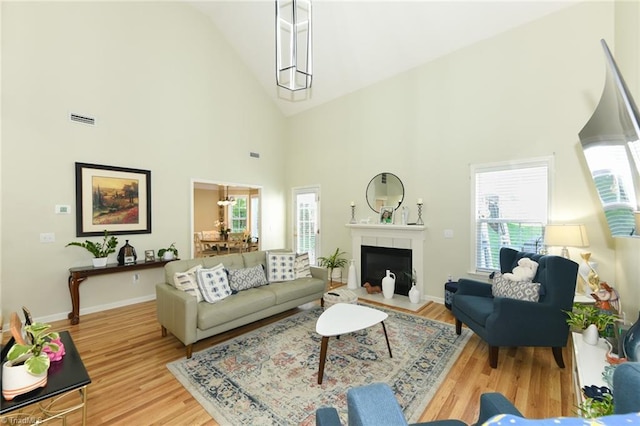 living area featuring healthy amount of natural light, high vaulted ceiling, wood finished floors, baseboards, and a fireplace