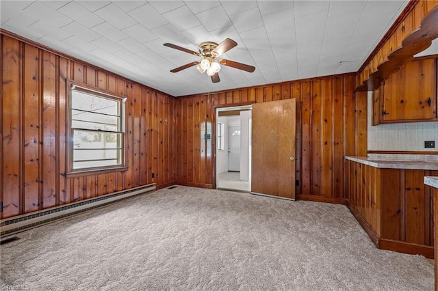unfurnished living room with a baseboard heating unit, a ceiling fan, wood walls, and carpet floors