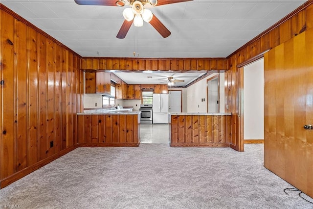 kitchen with a ceiling fan, brown cabinetry, light colored carpet, stove, and freestanding refrigerator