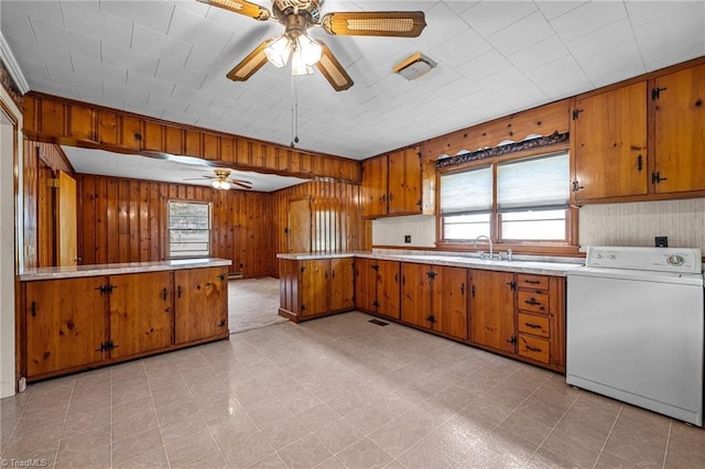 kitchen with a peninsula, a ceiling fan, brown cabinets, and washer / clothes dryer
