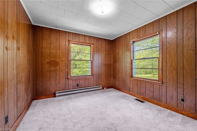 carpeted empty room with a baseboard radiator, a healthy amount of sunlight, wood walls, and baseboards