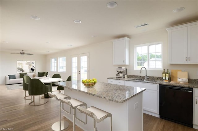 kitchen featuring light stone countertops, a center island, white cabinetry, black dishwasher, and sink