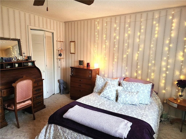 carpeted bedroom with wallpapered walls, ceiling fan, a closet, and a textured ceiling