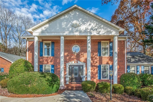 greek revival house with covered porch, brick siding, and a chimney