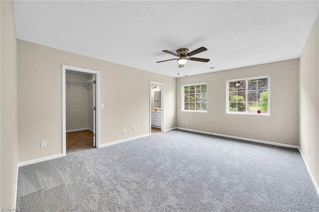 unfurnished bedroom featuring ceiling fan, light carpet, a closet, and a walk in closet