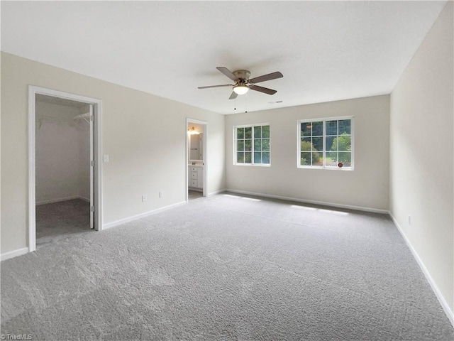 unfurnished bedroom featuring a closet, ceiling fan, ensuite bath, a walk in closet, and light colored carpet