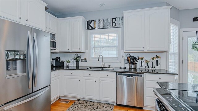 kitchen with white cabinets, sink, appliances with stainless steel finishes, and light hardwood / wood-style flooring