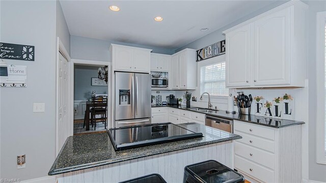 kitchen with dark stone counters, stainless steel appliances, sink, white cabinetry, and a kitchen island