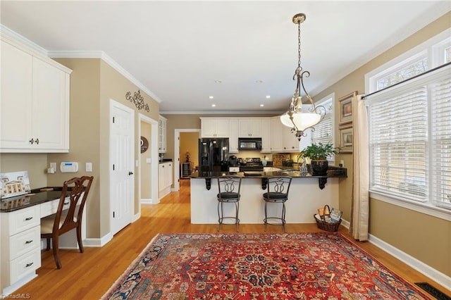 kitchen with kitchen peninsula, hanging light fixtures, white cabinets, black appliances, and built in desk