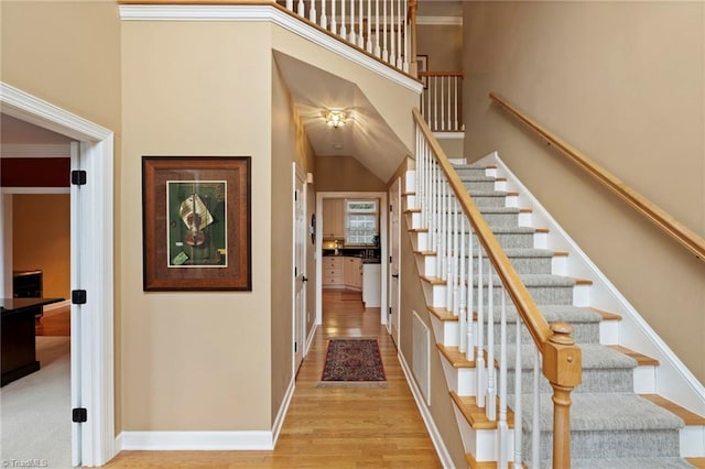 staircase featuring wood-type flooring, crown molding, and a towering ceiling