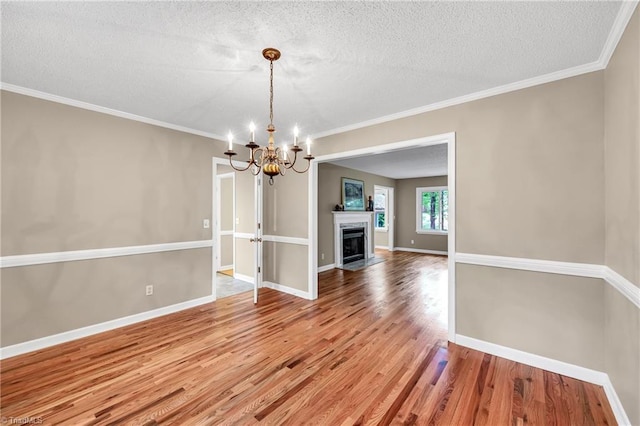 unfurnished dining area featuring wood finished floors, a chandelier, a textured ceiling, crown molding, and baseboards