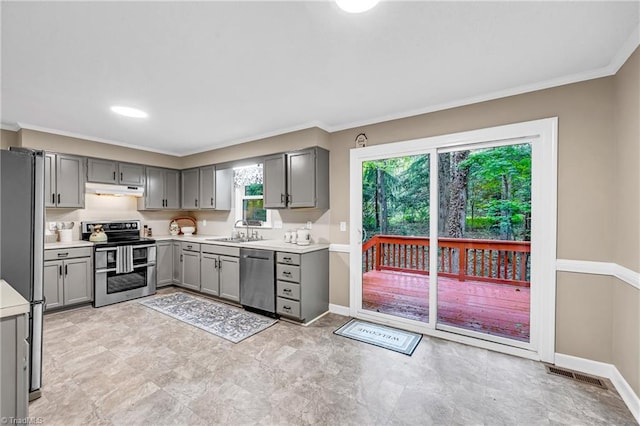 kitchen featuring appliances with stainless steel finishes, gray cabinets, under cabinet range hood, crown molding, and light countertops