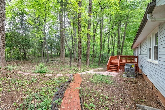 view of yard featuring a deck, central AC unit, and a view of trees