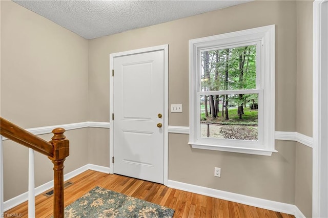 foyer entrance featuring baseboards, wood finished floors, and a textured ceiling