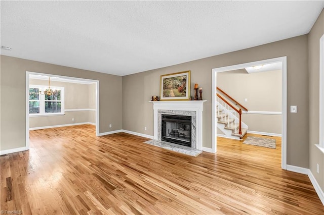unfurnished living room featuring light wood-style flooring, a textured ceiling, stairs, a premium fireplace, and baseboards