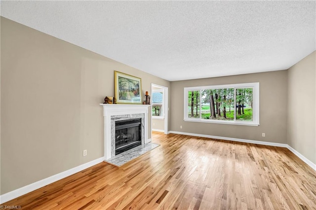 unfurnished living room with light wood finished floors, a textured ceiling, a premium fireplace, and baseboards