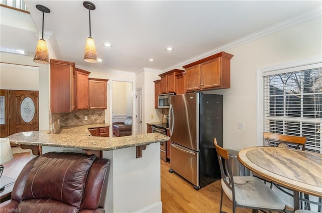 kitchen featuring light wood-type flooring, appliances with stainless steel finishes, decorative light fixtures, kitchen peninsula, and a breakfast bar area