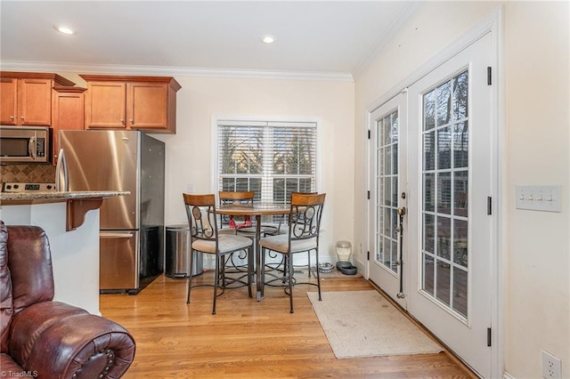 kitchen featuring tasteful backsplash, a kitchen breakfast bar, crown molding, appliances with stainless steel finishes, and light wood-type flooring