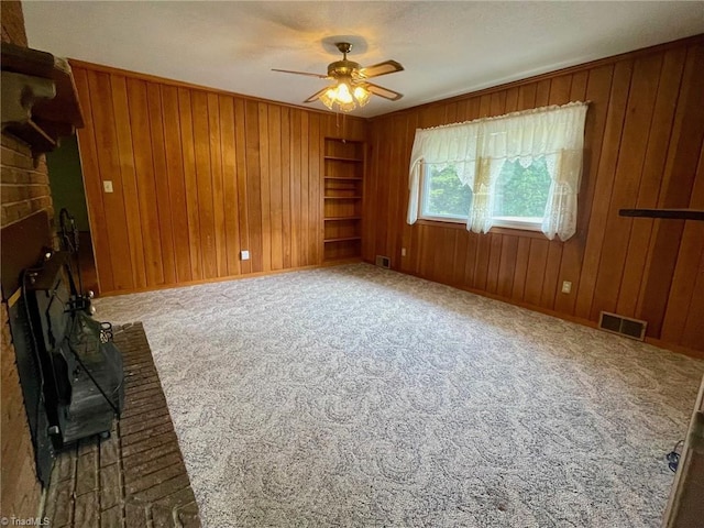 unfurnished room featuring wood walls, a brick fireplace, carpet flooring, and visible vents