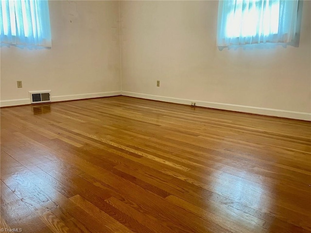 unfurnished room featuring a healthy amount of sunlight, baseboards, visible vents, and wood finished floors