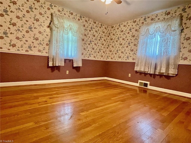 empty room with wallpapered walls, visible vents, and a wainscoted wall