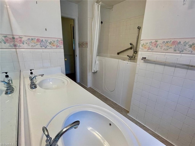 bathroom featuring a garden tub, tile walls, a sink, and a wainscoted wall