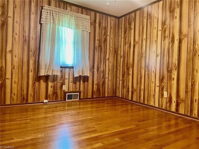 empty room featuring visible vents, wood walls, and wood finished floors