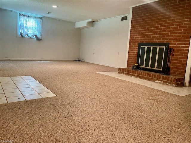 below grade area featuring a textured ceiling, carpet floors, a brick fireplace, and visible vents