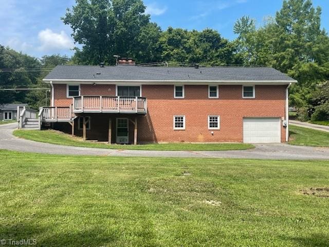 rear view of property with an attached garage, a deck, a lawn, and brick siding