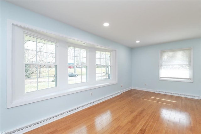 unfurnished room featuring baseboard heating, wood-type flooring, and a wealth of natural light