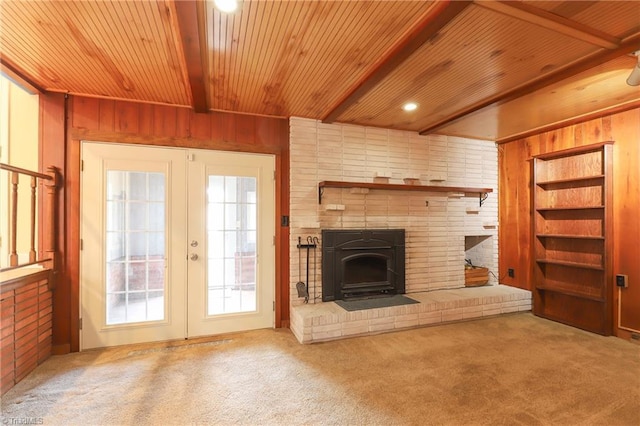 unfurnished living room with wood walls, carpet flooring, wood ceiling, french doors, and beamed ceiling