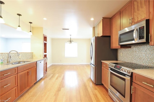 kitchen featuring stainless steel appliances, brown cabinets, a sink, and light wood-style flooring