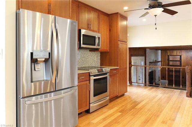 kitchen featuring brown cabinets, tasteful backsplash, light countertops, appliances with stainless steel finishes, and light wood-style floors