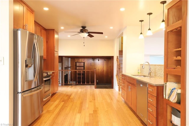 kitchen with light wood-type flooring, appliances with stainless steel finishes, brown cabinetry, and a sink