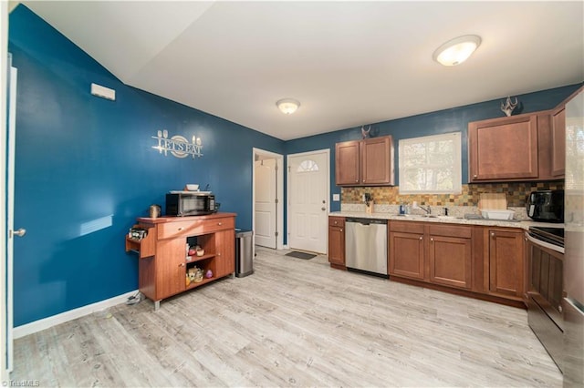 kitchen with sink, appliances with stainless steel finishes, light wood-type flooring, and backsplash