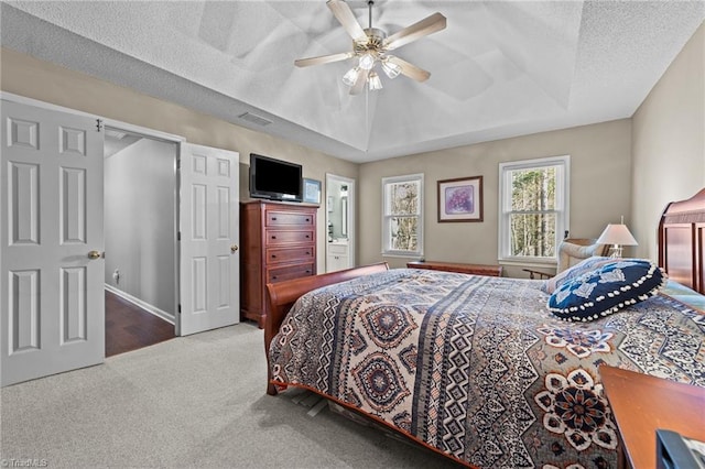 carpeted bedroom featuring a raised ceiling, ceiling fan, a textured ceiling, and connected bathroom