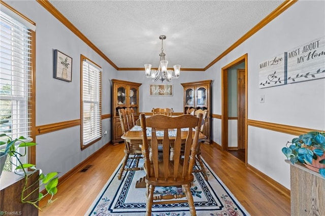 dining room featuring a notable chandelier, light hardwood / wood-style floors, a textured ceiling, and ornamental molding