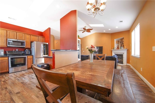 dining space featuring ceiling fan with notable chandelier, light hardwood / wood-style floors, and vaulted ceiling with skylight