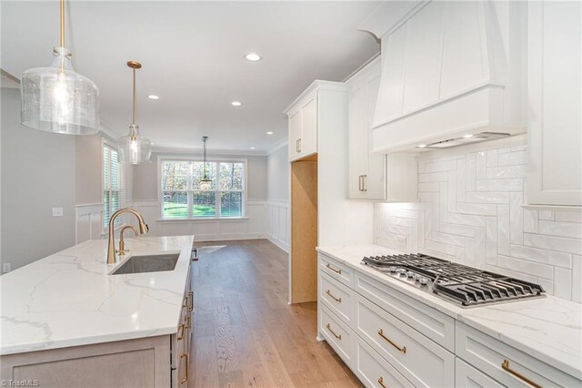 kitchen with sink, white cabinetry, a kitchen island with sink, light stone counters, and decorative light fixtures