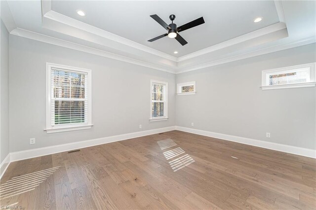 empty room featuring wood-type flooring, ceiling fan, crown molding, and a tray ceiling