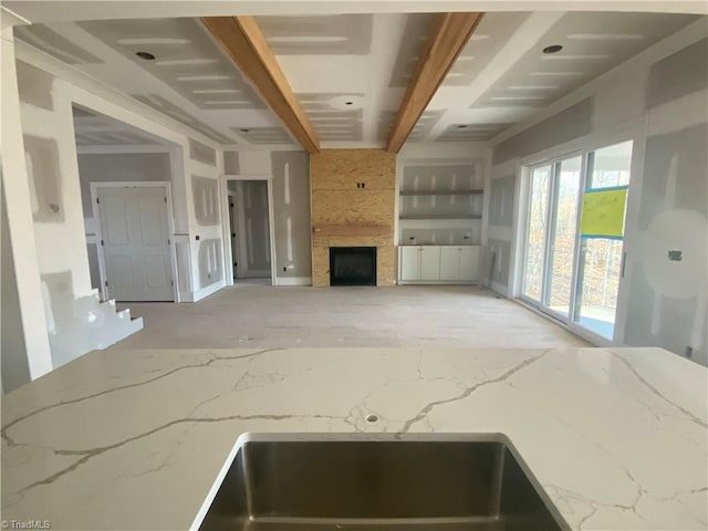 kitchen featuring beam ceiling, a fireplace, and light stone countertops