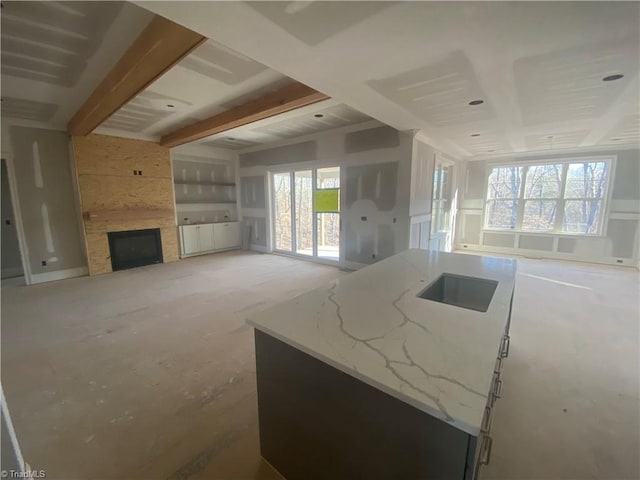 kitchen with sink, light stone counters, a large fireplace, a kitchen island, and beam ceiling