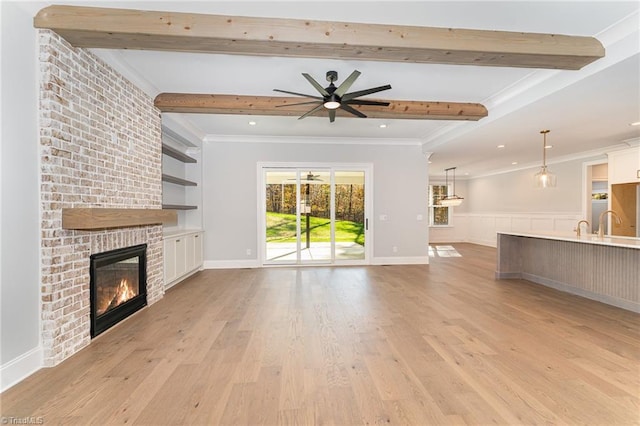 unfurnished living room with a brick fireplace, light hardwood / wood-style flooring, ornamental molding, beamed ceiling, and ceiling fan