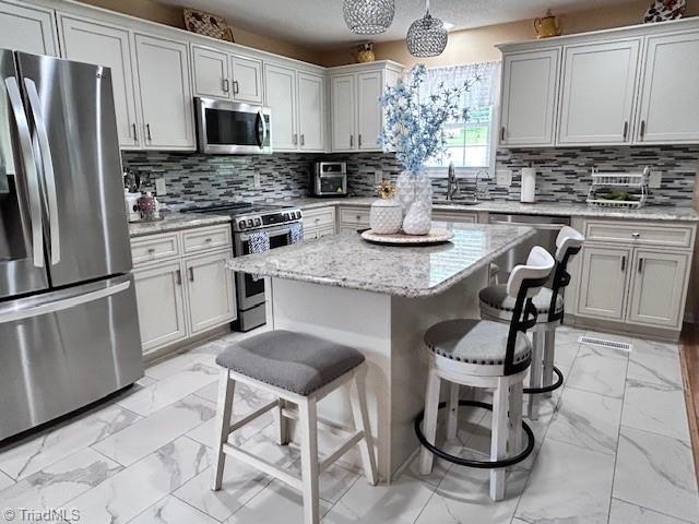 1320 Little Gate Dr, Asheboro, NC 27205 - kitchen with appliances with stainless steel finishes, light marble finish floors, a kitchen breakfast bar, a kitchen island, and tasteful backsplash