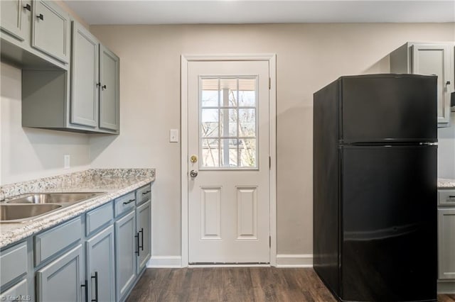 kitchen with baseboards, dark wood-type flooring, freestanding refrigerator, gray cabinets, and a sink