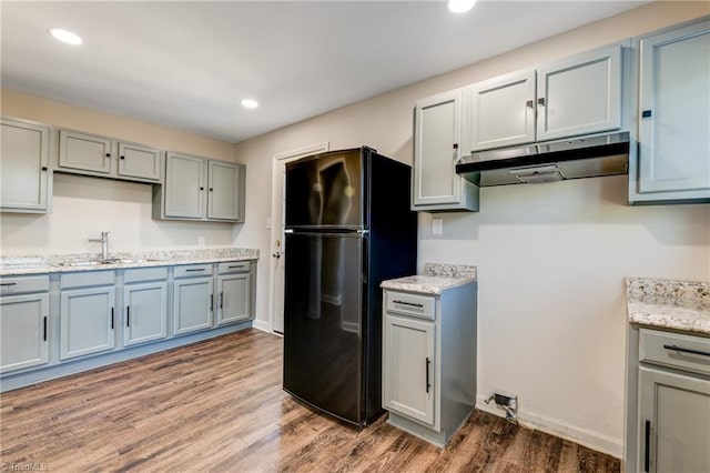 kitchen featuring gray cabinetry, under cabinet range hood, a sink, wood finished floors, and freestanding refrigerator