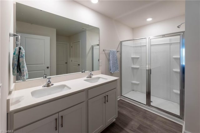 bathroom with double vanity, wood finished floors, a stall shower, and a sink