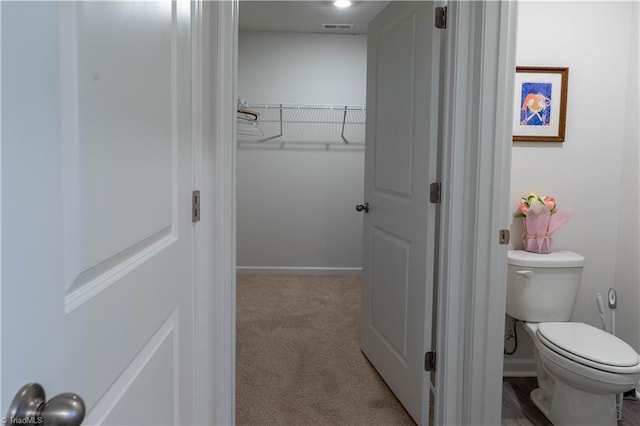 bathroom featuring toilet, baseboards, visible vents, and a walk in closet