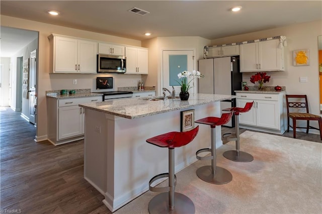 kitchen with recessed lighting, stainless steel microwave, white cabinets, a sink, and a kitchen breakfast bar