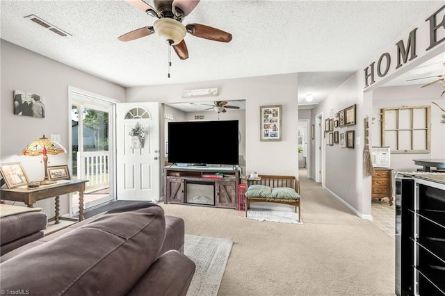living area featuring visible vents, carpet floors, baseboards, ceiling fan, and a textured ceiling